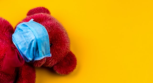Un oso de peluche rojo cubre su boca y nariz con una mascarilla higiénica.