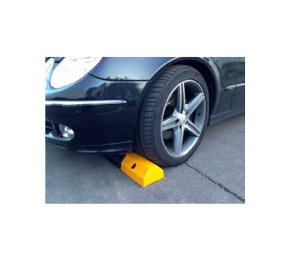 Una rueda de coche se apoya en un tope de parking amarillo y negro